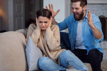 Defenseless upset woman closes her ears while her husband yelling at her sitting behind. Family relationship problems concept.の写真素材