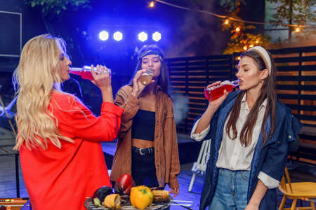 Three pretty girls drink cocktails or energy drinks at outdoors nightclub party.の写真素材