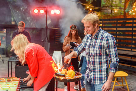 Handsome man is grilling delicious food on grill for his friends at barbecue party outdoors. Picnic time, weekend. Slow motionの写真素材