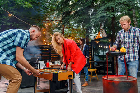 Handsome man grilling vegetables, other friends talking together near dj and one guy and girl play...