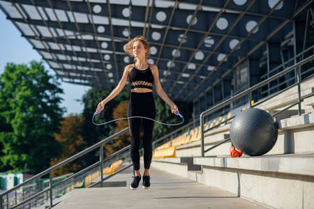 Woman jumping with skipping rope at stadium. Active fitness female doing exercises outdoor. Fitness...