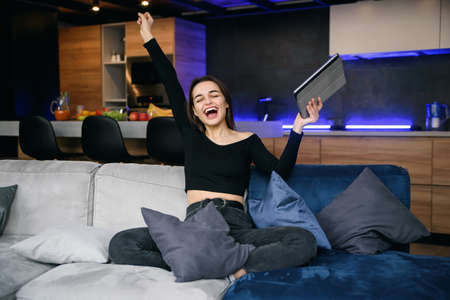 Young attractive woman at a modern office desk, with laptop, stretching her arms with extreme joy...