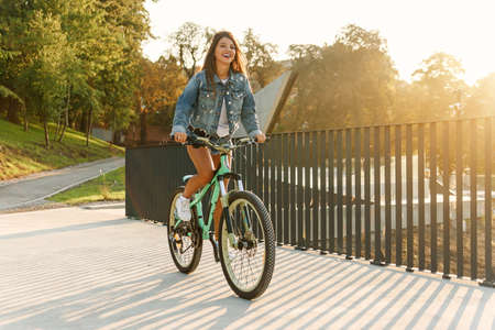 Young stylish caucasian girl rides bicycle on the city rooftop at sunrise.の写真素材