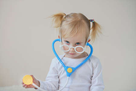 Joyful toddler girl playing as a doctor and hospital using stethoscope toy having fun at home.の写真素材