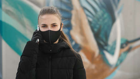 Young girl in city street wearing black sterile medical face mask. Woman using the phone to search for news about nCov 2019. Quarantine COVID-19 pandemic coronavirus epidemic and health care conceptの写真素材
