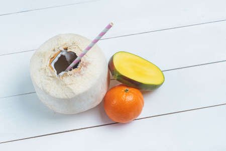Fresh coconut with straw, half of mango and mandarin on white background. Top view.の写真素材