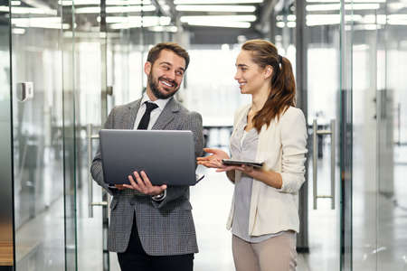 Businesswoman and businessman in laptop standing and discussing project in empty office windows with...