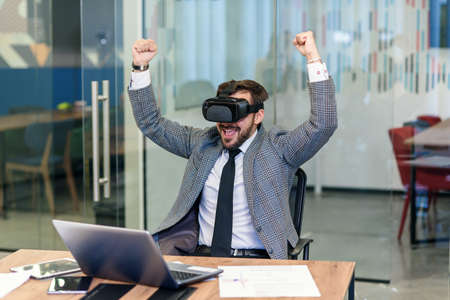 A young office male worker raises his hands and happily exclaimed with new experiences using augmented reality glasses. Innovation technologies in business.の写真素材