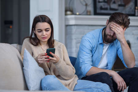 Modern couple at home. Man and woman concentrated on messaging with smartphones, ignoring each other and spending time on social media.の写真素材