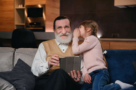 Slow motion of cute joyful 12-aged girl with funny pigtails which whispering on granddads ear her...
