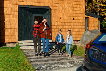 Handsome bearded man makes a surprise for his beautiful brunette wife. A happy man closes the girlfriends eyes with his hands and leads her to a new black car.の写真素材