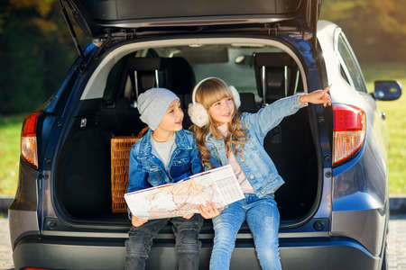 Agreeable boy and girl are looking at the road map while sitting in the autos trunk and discussing the move direction. Family vacation trip by car.の写真素材