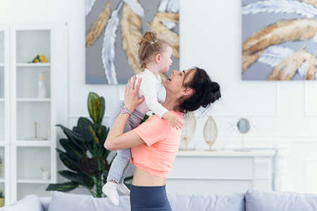 Young beautiful mother having fun with her toddler daughter at cozy home.