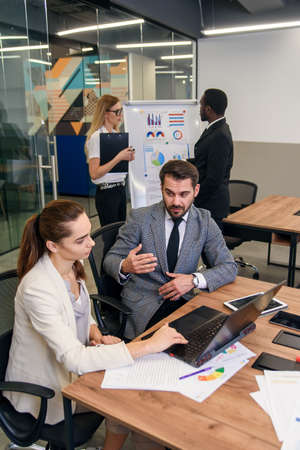 Joined work of two confident business people in formal suit working together with laptop at office...