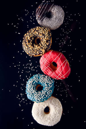 Multicolored decorated doughnuts in motion falling on brown background. Sweet donuts flying in motion.の写真素材