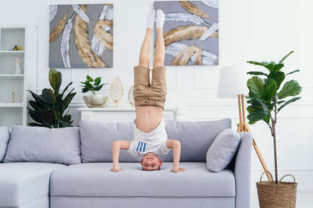 Adorable child standing on his head on sofa at home stock photoの写真素材