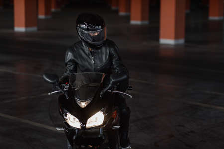 Girl in black protective uniform, gloves and full-face helmet riding on her motorcycle on...