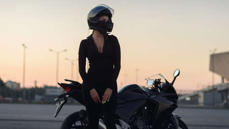 Pretty biker woman with beautiful eyes in black leather jacket and full-face protective helmet sits...