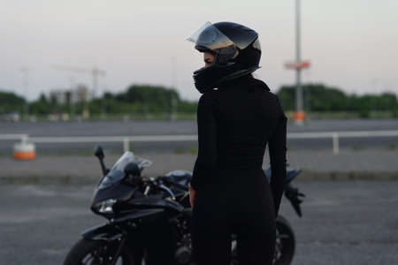 Biker woman in black leather jacket and full face helmet sits near stylish sports motorcycle at urban parking. Traveling and active lifestyle concept.の写真素材