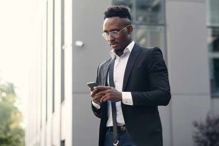 Serious black businessman texting on smartphone outdoors. Young african-american salesman working...