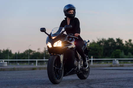 A beautiful biker girl leaning on her superbike outside a building.の写真素材