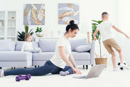 Mother meditating making yoga exercises while active energetic children playing on background. Mom doing yoga exercise at home for stress relief relaxing with naughty kids.の写真素材