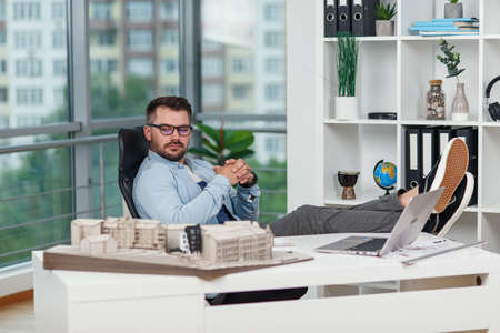 Happy office male worker in casual clothes laid his feet on workspace table while dreaming about...