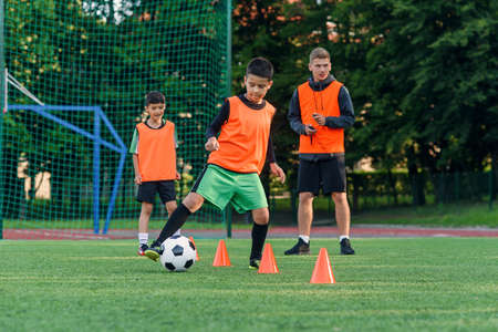 Persistent teen boy in sportswear trains football on soccer field and learns to circle the ball between training cones.の写真素材