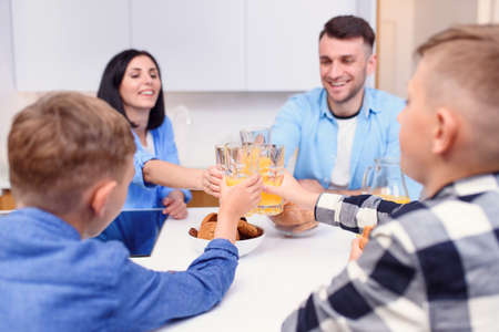 Joyful stylish family with two sons drink orange juice with cakes in the modern kitchen. Happy family concept.の写真素材