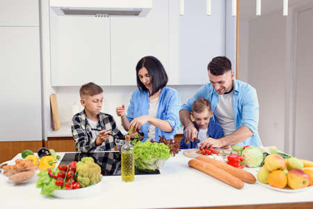 Happy stylish family having fun while preparing healthy vegetables breakfast in modern bright kitchen together.の写真素材