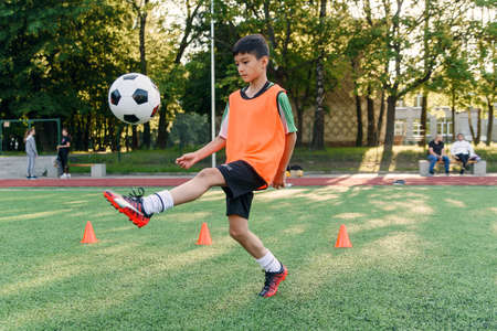 Motivated teen football player stuffs soccer ball on leg. Practicing sport exercises at artificial stadium.の写真素材