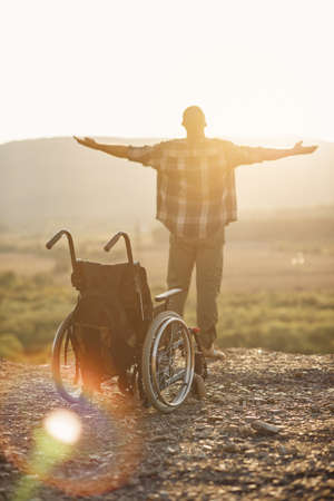 The concept of healed disabled people. A young man got up to his legs from a wheelchair on top of a mountain at sunrise.の写真素材