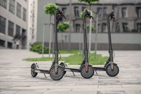 Three modern stylish black electric scooter are parked near big office centre. Electricity and eco...