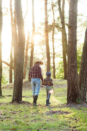 Back view likable bearded grandpa in forest going fishing together with his 10-aged grandson and talking about fishing.の写真素材