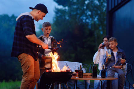 Happy father and son preparing a barbecue on a family vacation on the terrace of their modern house in the evening.の写真素材