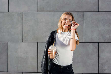 Beautiful happy girl with cold fresh smoothie outdoors. Smiling hipster girl with cup of milkshake...