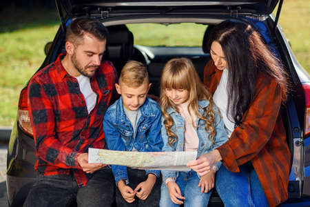 Close up of joyful pleasant family which gethering on their vacation with teen children and using road map to choose the right path on the carの写真素材