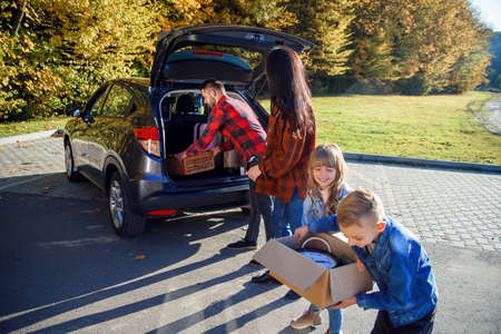 High-spirited likable parents unloading the autos trunk with their cute 10-12s kids during moving into new apartment.の写真素材