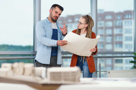 Confident stylish bearded male designer and his female colleague with dreadlocks analysing printed on paper project.の写真素材