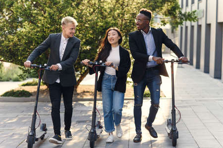 Joyful multiracial colleagues discussing details of business project go to office with electric scooters.の写真素材
