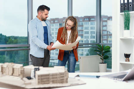 Confident stylish bearded male designer and his female colleague with dreadlocks analysing printed on paper project.の写真素材