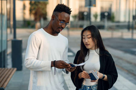 Happy multiracial couple look at boarding pass checking departure time at the stop near airport....
