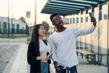 Cheerful multiracial male and female friends making selfie on smartphone with passports and tickets before joint trip.の写真素材