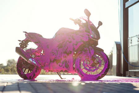 Stylish sports motorcycle with purple foam on the self-service car wash at sunrise.の写真素材