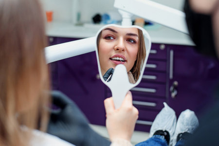 Young woman patient looking at mirror and admires her new smile after dental treatment in the...