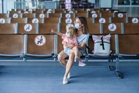 Mother with daughter in masks waiting for their flight at airport. Woman with little girl in international airport.の写真素材