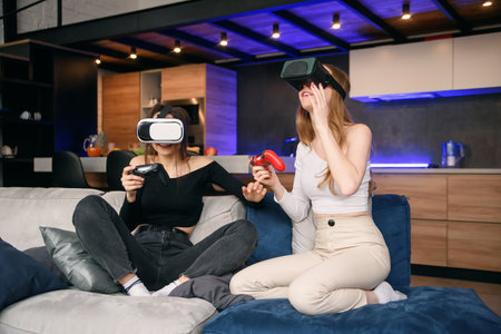 Girlfriends playing with excitement video games at home using vr glasses. Enjoying vacation time to spend leisure with friends.の写真素材