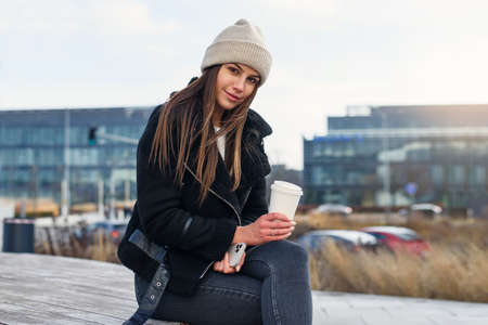 Smiling pretty woman with smart phone and coffe to go standing outdoors and speaking. Modern lifestyle concept.の写真素材