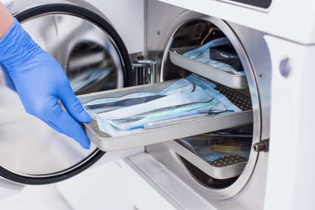 Assistants hand in gloves insert packaged dental instrument to the autoclave to sterilise.の写真素材