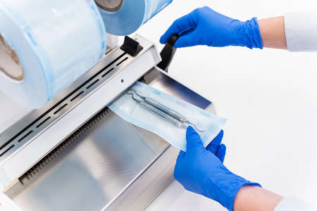Dentist assistant packing dental equipment in plastic sterilization pouches after autoclave....